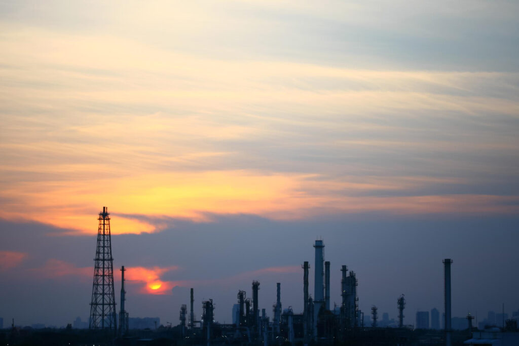 Силуэт нефтеперерабатывающего завода на фоне вечернего неба с промышленными колоннами и технологическими сооружениями.